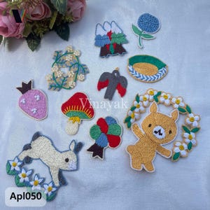 May include: A collection of embroidered patches in various shapes, including a strawberry, mushroom, bird, and bear. The patches feature bright colors and detailed stitching. The text "Vinayak" and "Apl050" are visible.