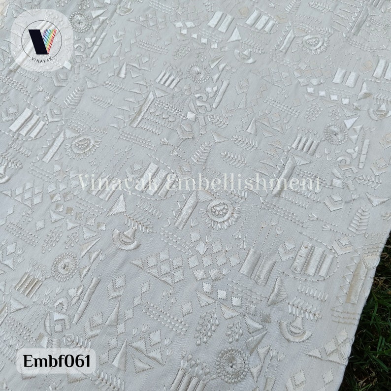 May include: White fabric with a geometric pattern embroidered in white thread. The fabric has a subtle texture and the embroidery is detailed and intricate. The fabric is called "Embf061".