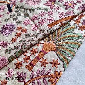 May include: A beige fabric with intricate embroidery featuring pink flowers, green leaves, and a brown tree with orange and green details. The fabric has the text "Embf038" in the bottom left corner.