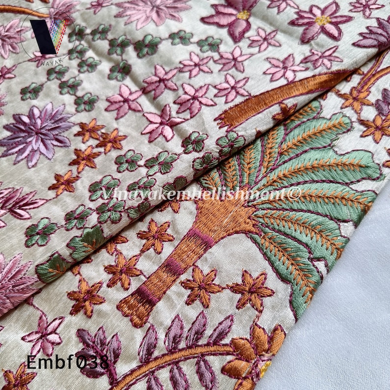 May include: A beige fabric with intricate embroidery featuring pink flowers, green leaves, and a brown tree with orange and green details. The fabric has the text "Embf038" in the bottom left corner.