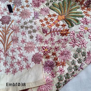 May include: A close-up of a cream-coloured fabric with pink, green and orange embroidered floral designs. The fabric is folded in half, and the embroidery is visible on both sides. The text "Embf038" is visible in the bottom left corner of the image.