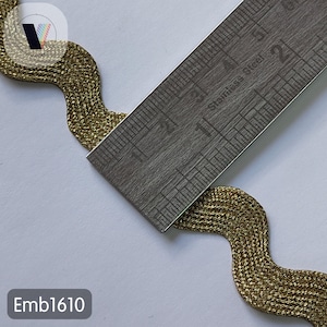May include: Close-up of a gold-colored, wavy trim with a metallic sheen. A stainless steel ruler is placed across the trim. The trim appears to be approximately 1 inch wide. The text "Emb1610" is in the lower left corner.