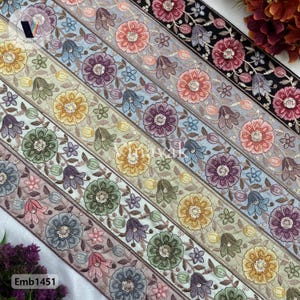 Könnte beinhalten: Sortiment aus sechs bestickten Besatzbändern mit Blumendesigns in verschiedenen Farben, darunter Rosa, Blau, Grün und Gelb. Die Bänder sind in einem geschichteten Muster angeordnet, wobei das breiteste Band unten und das schmalste Band oben liegt.
