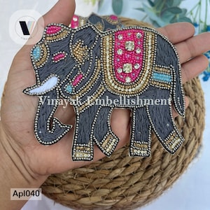 Könnte beinhalten: Graue bestickte Elefanten-Applikation mit bunten Perlen und Strasssteinen. Der Elefant hat einen weißen Stosszahn und ist mit goldenen und blauen Akzenten verziert. Die Applikation ist perfekt, um Ihren Bastelarbeiten einen Hauch indischer Kultur zu verleihen.