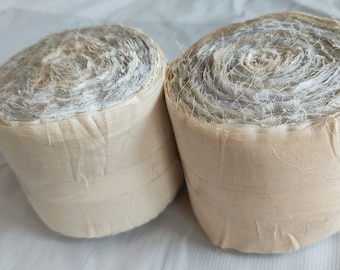 May include: Two rolls of beige fabric with a white, sheer, mesh-like texture. The fabric is rolled tightly and the ends are secured with a beige thread.