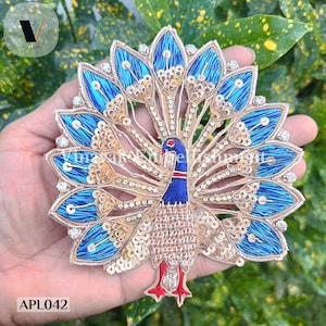 May include: A blue and gold peacock applique with a spread tail, embellished with sequins and rhinestones. The applique is approximately 6 inches in diameter.  APL042