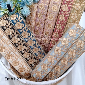 May include: Assortment of embroidered trim in various colours, including blue, black, white, pink, red, and gold. The trim features a floral design with gold thread embroidery. The trim is displayed in a wicker basket. Emb1127