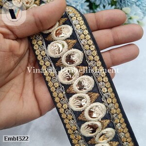 May include: Black trim with gold and silver embellishments. The trim features a repeating pattern of oval-shaped sequins and small floral designs. The trim is approximately 5 cm wide.