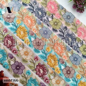 May include: Assortment of embroidered trim with floral designs in various colors, including turquoise, gold, pink, and gray. The trim is on a sheer white fabric.