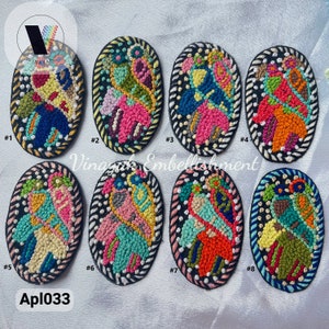 May include: Eight oval-shaped embroidered patches with colorful abstract designs. The patches are numbered 1 through 8. The text "Vinayak Embellishment" and "Apl033" are visible in the image.