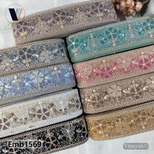 May include: A selection of embroidered lace ribbons in shades of purple, teal, pink, and gold. Each ribbon displays floral designs and decorative elements. The text "Emb 1569" is present on one of the ribbons.