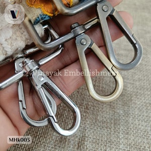 May include: Three metal clasps, one silver and two antique gold, with a close-up view of the silver clasp. The clasps are attached to a fabric background.