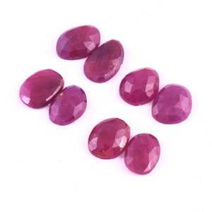 May include: Eight oval-shaped, faceted ruby gemstones. The rubies are a deep pink colour and have a glossy finish.