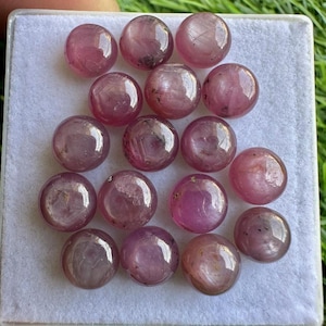 May include: A collection of 15 pink cabochon gemstones, each with a smooth, rounded surface. The stones are arranged in a random pattern on a white background.