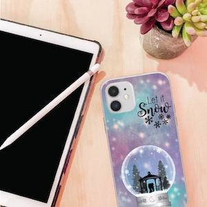 May include: A white phone case with a winter-themed design. The case features a snow globe with a couple inside a gazebo, surrounded by trees. The text "Let it Snow" is written in black cursive with snowflakes.