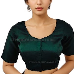 Könnte beinhalten: Eine dunkel smaragdgrüne Bluse mit kurzen Ärmeln und einem Rundhalsausschnitt. Die Bluse hat einen satinartigen Glanz und eine dezente vertikale Naht auf der Vorderseite. Der Text "ETHNICFASHIONSTORE" ist auf der Bluse aufgedruckt.