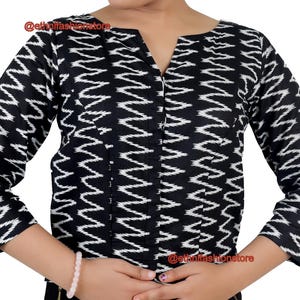 May include: Black and white patterned top with a V-neck and three-quarter sleeves. The top has a zigzag design. The sleeves extend to the elbows. The top is made of a soft material.