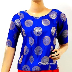 Puede incluir: Una blusa azul real con cuello redondo y mangas cortas. La blusa está adornada con un patrón repetido de diseños circulares plateados.