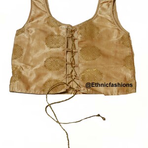May include: A gold sleeveless top with a lace-up front and a gold floral pattern. The top has a scoop neck and is made of a silky fabric. The text "@Ethnicfashions" is visible in the bottom right corner of the image.