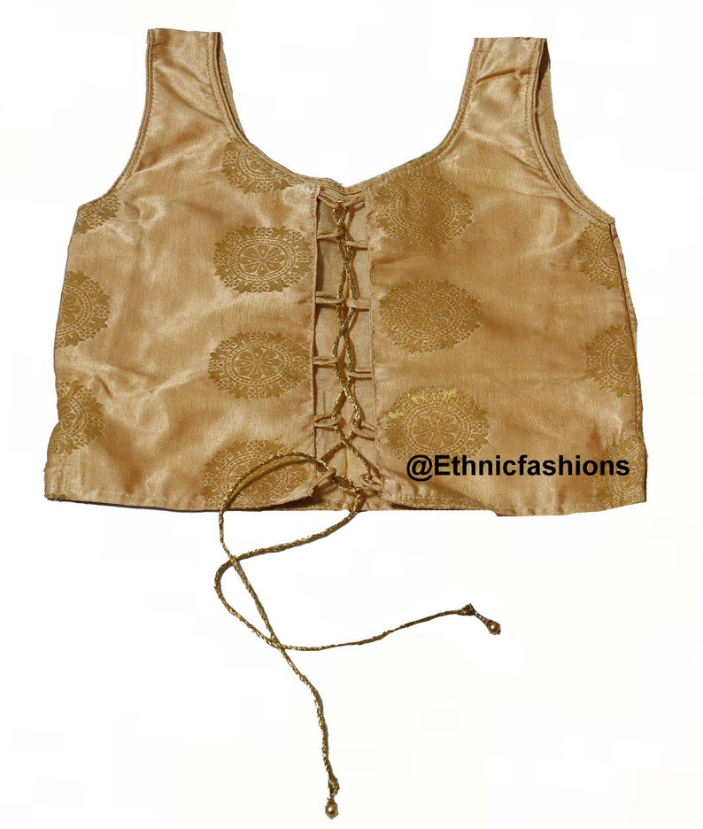 May include: A gold sleeveless top with a lace-up front and a gold floral pattern. The top has a scoop neck and is made of a silky fabric. The text "@Ethnicfashions" is visible in the bottom right corner of the image.