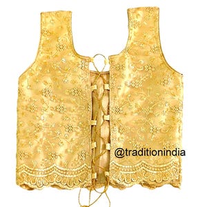 May include: A gold embroidered sleeveless blouse with a lace trim and a lace-up back. The blouse is decorated with floral patterns and sequins. The text "@traditionindia" is visible on the bottom right corner of the blouse.