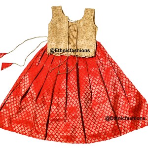May include: A red and gold sleeveless dress with a lace-up bodice and a full skirt. The skirt has a floral pattern and the bodice is embroidered. The dress is perfect for a special occasion.