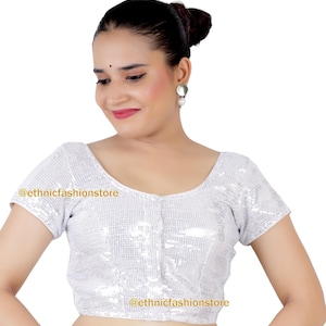 Puede incluir: Una blusa de lentejuelas plateadas con mangas cortas y escote redondo. La blusa tiene un estilo ajustado y es corta a la cintura. El texto "@ethnicfashionstore" es visible en la blusa.