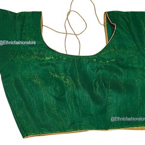 May include: A green blouse with short sleeves and a scoop neckline. The blouse has gold trim along the neckline and sleeves. The text "@Ethnicfashionstore" is visible on the garment.