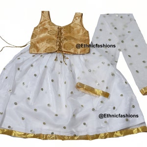May include: A white and gold girls' lehenga choli with a gold embroidered bodice and a white skirt with sequins. The skirt has a gold trim and the set includes a white dupatta with gold trim. The text '@Ethnicfashions' appears twice on the image.