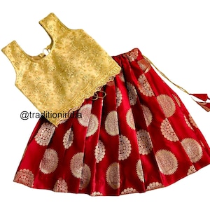 May include: A red and gold skirt and top set for a young girl. The skirt has a gold pattern of circles and the top is gold with a lace trim.
