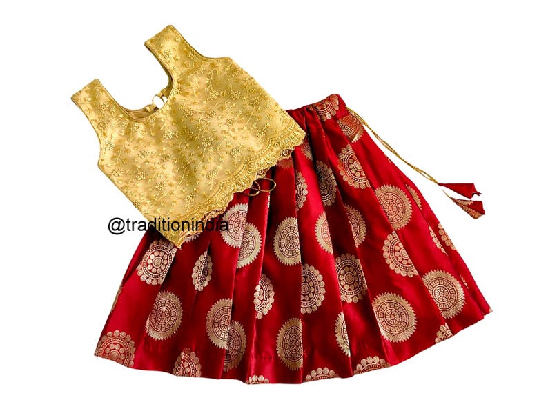 May include: A red and gold skirt and top set for a young girl. The skirt has a gold pattern of circles and the top is gold with a lace trim.