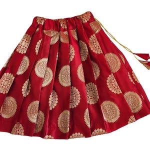 May include: Red skirt with gold circular patterns. The skirt has pleats and a drawstring closure with a tassel.