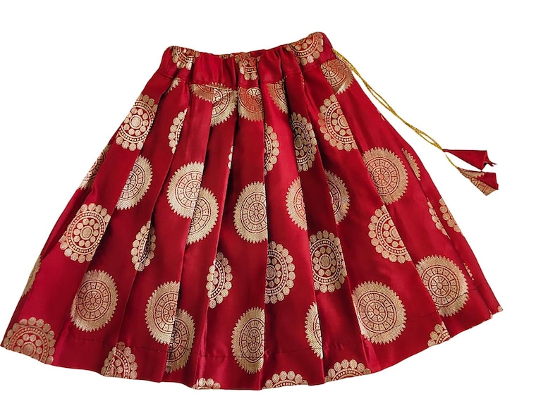 May include: Red skirt with gold circular patterns. The skirt has pleats and a drawstring closure with a tassel.