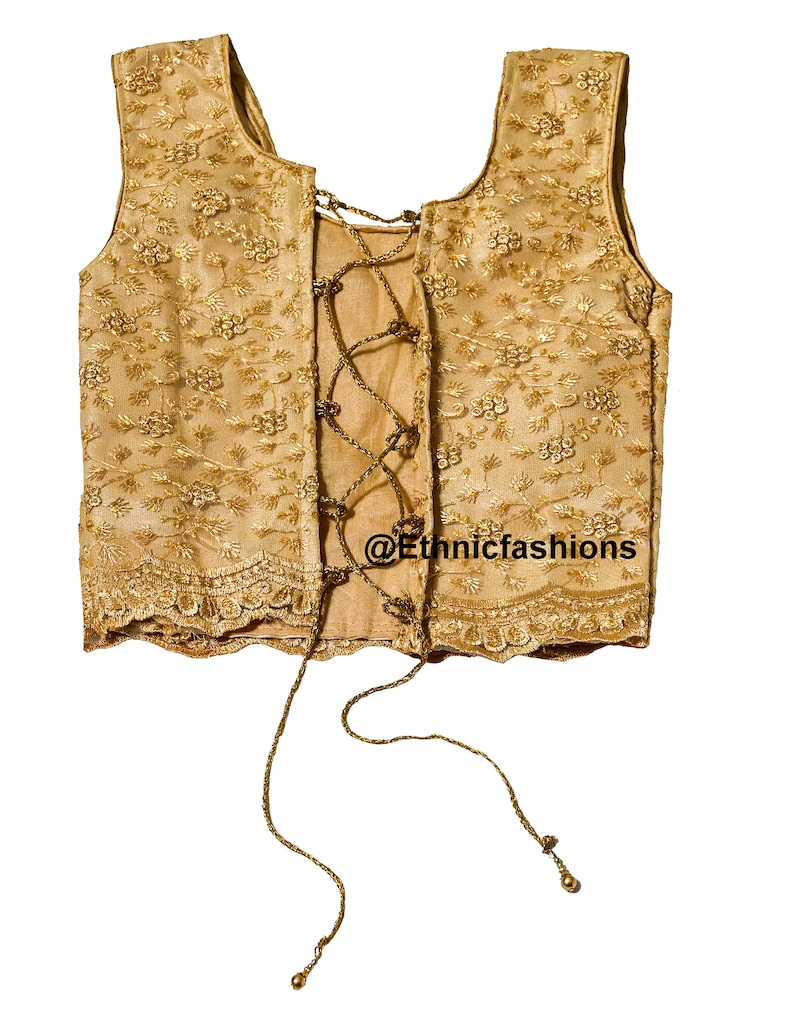 May include: A gold sleeveless blouse with a lace-up back and floral embroidery. The blouse has a scalloped hem and is tied with a gold cord.