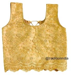 May include: A gold embroidered sleeveless blouse with a scalloped hem. The blouse features a floral pattern and a tie-back detail.