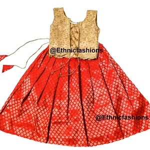 May include: A red and gold sleeveless dress with a lace-up back. The dress has a gold embroidered bodice and a red skirt with a gold pattern. The dress is tied at the waist with a gold cord. The dress is tagged with the text "@Ethnicfashions".