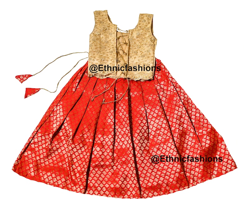May include: A red and gold sleeveless dress with a lace-up back. The dress has a gold embroidered bodice and a red skirt with a gold pattern. The dress is tied at the waist with a gold cord. The dress is tagged with the text "@Ethnicfashions".