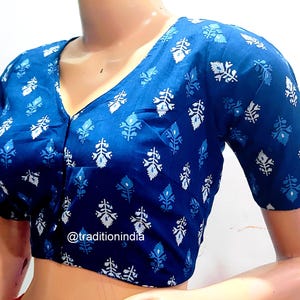 May include: A blue and white cotton blouse with a button-up front and short sleeves. The blouse has a floral pattern and the text "@traditionindia" is visible on the front.