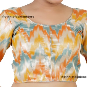 May include: A short-sleeved,  cream-colored blouse with a zig-zag pattern in shades of orange, yellow, and blue. The blouse has a button closure in the front and the text "@ethnicfashionstore" is printed on the fabric.