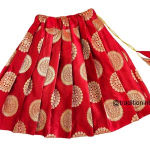 May include: Red skirt with gold circular patterns and a gold tassel. The skirt is pleated and has a drawstring waist.
