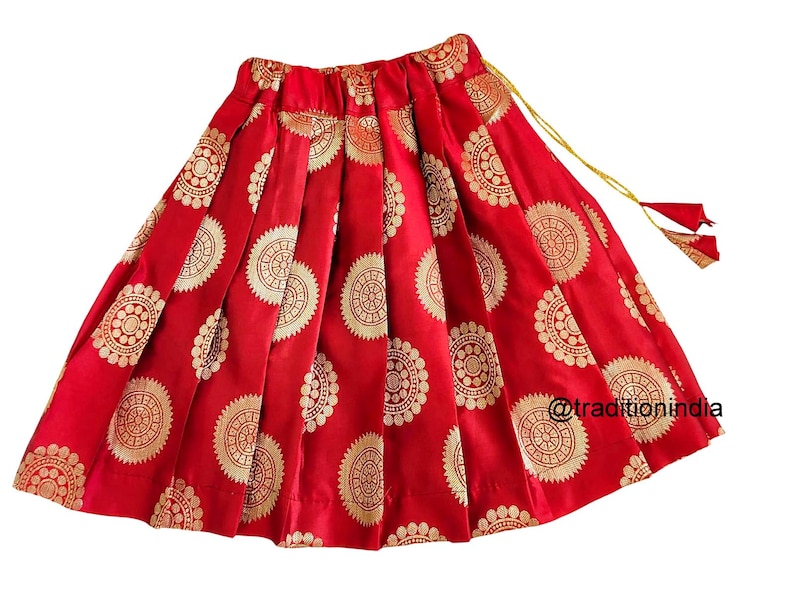 May include: Red skirt with gold circular patterns and a gold tassel. The skirt is pleated and has a drawstring waist.