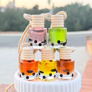 May include: Five small glass bottles with black polka dots and cork stoppers. The bottles are filled with different coloured liquids: pink, green, orange, yellow, and brown. The bottles are hanging from a string.