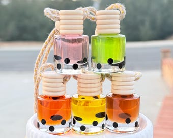 Könnte beinhalten: Fünf kleine Glasflaschen mit schwarzen Punkten und Korkstopfen. Die Flaschen sind mit verschiedenen Flüssigkeiten gefüllt: rosa, grün, orange, gelb und braun. Die Flaschen hängen an einer Schnur.