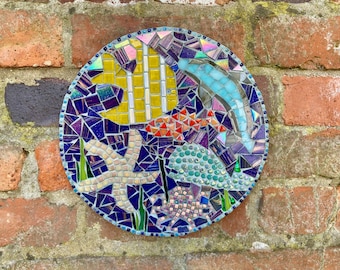 May include: A colorful mosaic wall art depicting a starfish, a fish, a dolphin, and seaweed. The mosaic is made of small, colorful tiles and is set against a brick background.