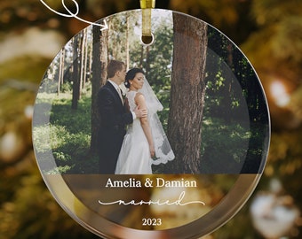 May include: A round glass ornament with a photo of a bride and groom in a forest setting. The ornament has a gold rim and the text "Amelia & Damian married 2023" printed on the bottom.