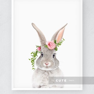 May include: A gray bunny with pink flowers in its fur, wearing a flower crown. The bunny is looking directly at the camera. The background is white.