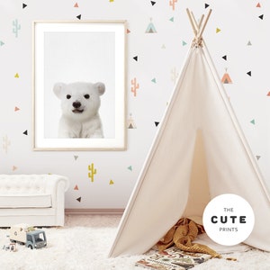 Puede incluir: Una tienda de campa&ntilde;a tipi blanca con una impresi&oacute;n de oso polar blanco en un marco en la pared detr&aacute;s de ella. La pared est&aacute; decorada con formas geom&eacute;tricas coloridas y pegatinas de cactus. La tipi est&aacute; sobre una alfombra blanca con una manta marr&oacute;n y amarilla en su interior.