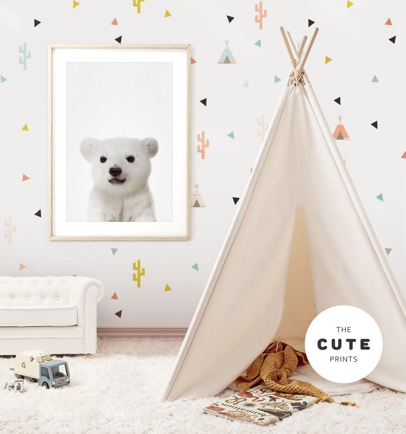 Puede incluir: Una tienda de campa&ntilde;a tipi blanca con una impresi&oacute;n de oso polar blanco en un marco en la pared detr&aacute;s de ella. La pared est&aacute; decorada con formas geom&eacute;tricas coloridas y pegatinas de cactus. La tipi est&aacute; sobre una alfombra blanca con una manta marr&oacute;n y amarilla en su interior.