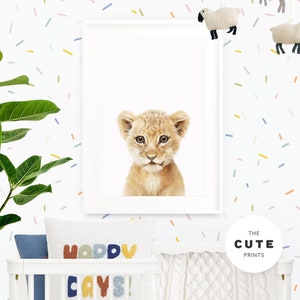 Peut inclure: Une impression encadr&eacute;e d'un adorable lionceau sur fond blanc. L'impression est accroch&eacute;e &agrave; un mur blanc avec des confettis multicolores. Le mur a &eacute;galement un lit b&eacute;b&eacute; avec une couverture en tricot blanc et un oreiller avec les mots "Happy Days!" en lettres color&eacute;es.
