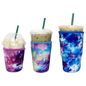 May include: Three different sizes of reusable coffee cup sleeves with tie-dye patterns in shades of blue, pink, and white. The sleeves are made of neoprene and are designed to keep drinks cold or hot.